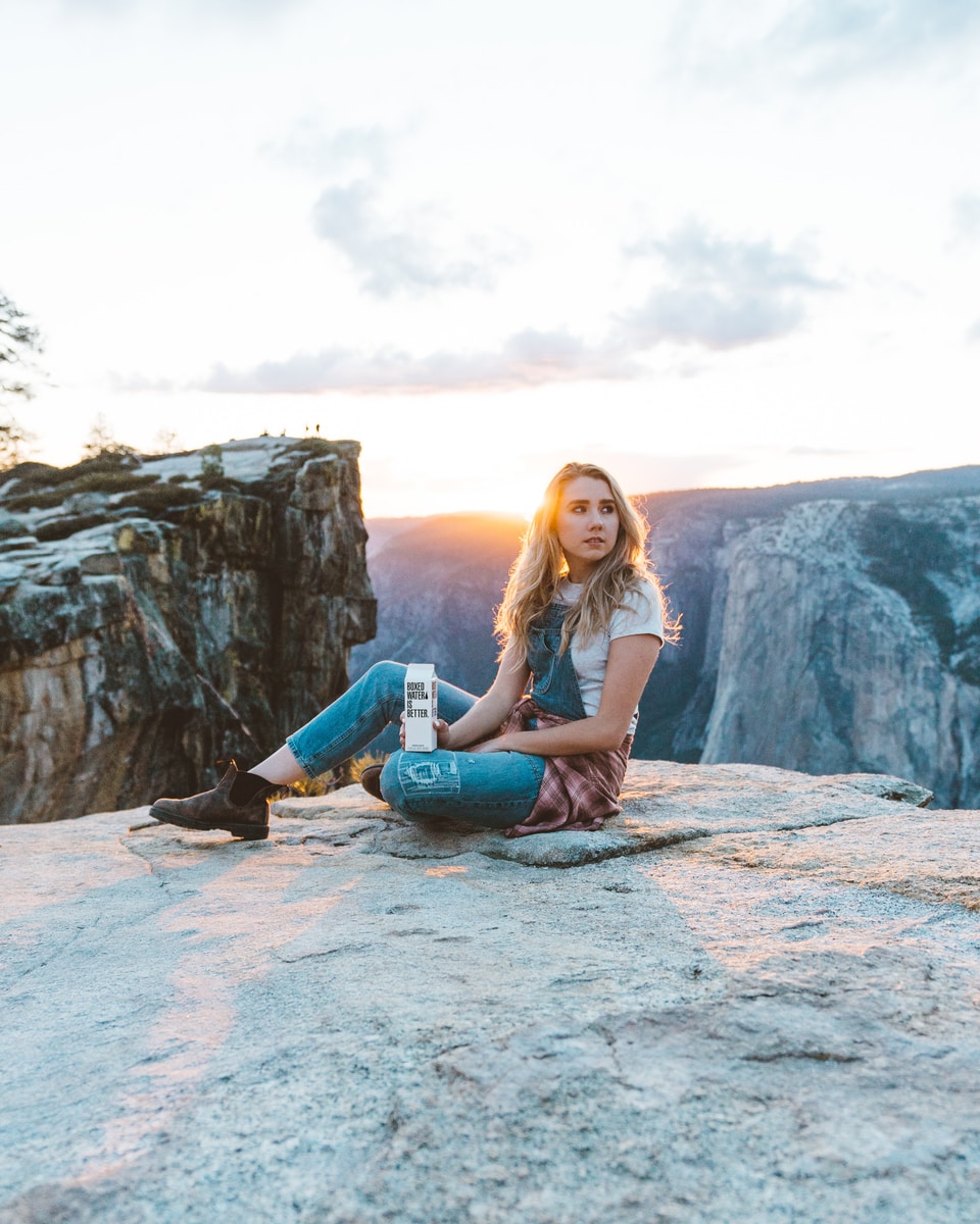 A woman sitting down in Yosemite holding a carton of Boxed Water